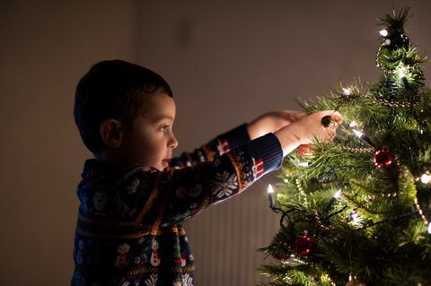 Băiat care decorează un pom de Crăciun acasă