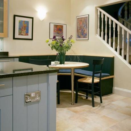 Banchetă de colț așezată la masă în bucătărie modernă cu unitate albastru pal și scară către etajul superior