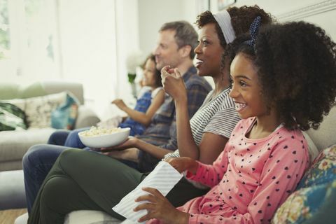 Tânără familie multi-etnică vizionând filme și mâncând floricele pe canapea
