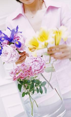 Femeie care aranjează flori tăiate într-o vază de sticlă