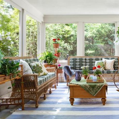 ecranat în verandă, covor cu dungi albastre și albe, scaune din răchită și canapea cu perne verzi și albe, plante de interior