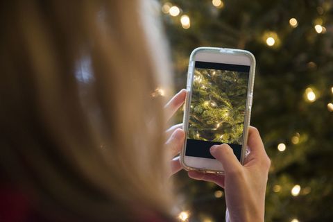 Femeie care fotografiază pomul de Crăciun cu telefonul mobil
