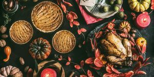 masa de cină de Ziua Recunoștinței cu pui întreg prăjit sau curcan mic, plăcintă cu dovleac pe fundal rustic întunecat cu farfurii, sos, tacâmuri, etichete pentru aranjarea mesei, lumânări aprinse, frunze roșii de toamnă, nuci și decor festiv, vedere de sus, natură moartă, plat culca